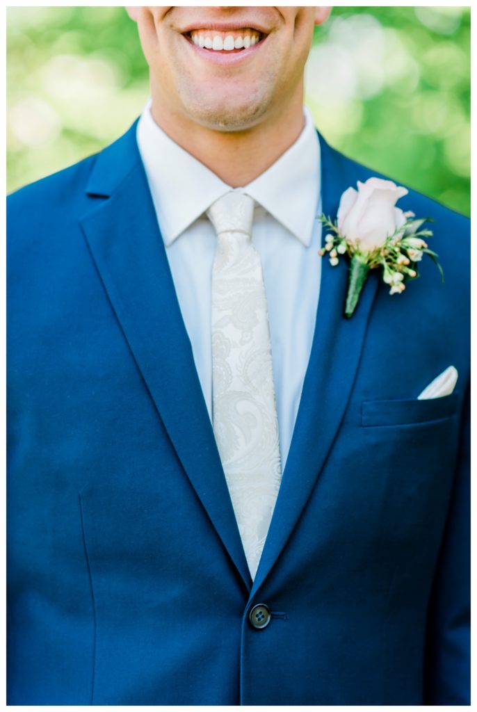 Smiling groom in a navy blue suit with  ivory tie and pocket square for this summer wedding. Suits by Milbern Clothing. Photo by Kayla Lee.