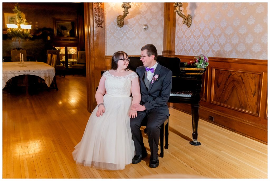 Bride and groom sit at a black piano, holding hands and smiling. This was at a Cotton Mansion winter wedding. It was taken using off camera flash. 