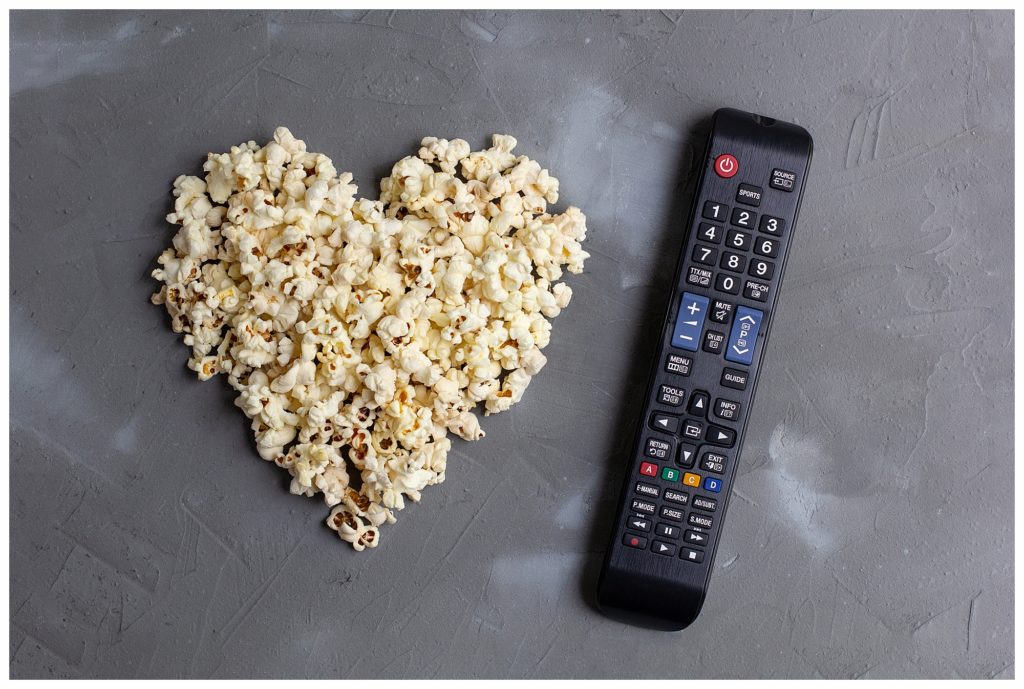 Popcorn in the shape of a heart and TV remote on grey stone background. Love movie. top view.